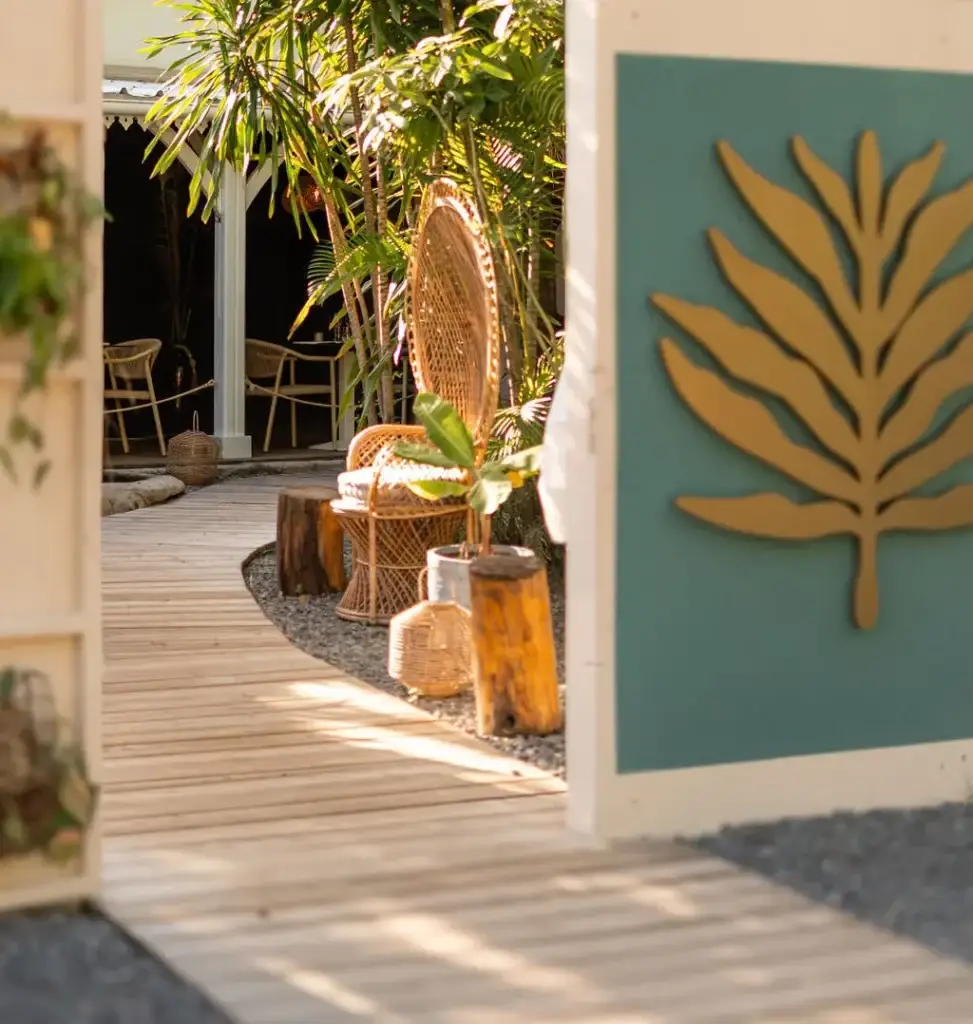 Chemin en bois menant à l'entrée du restaurant Boho avec fauteuil emmanuelle et logo mural végétal.